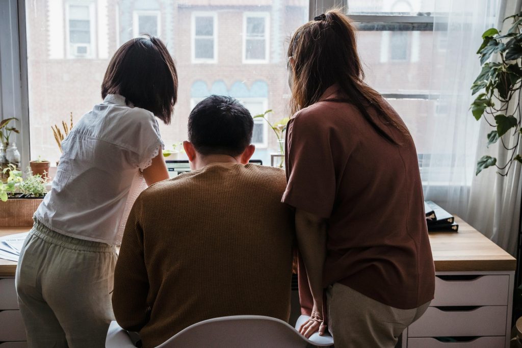 A group of three people collaborating at a desk in a sunlit office space with plants and natural light.