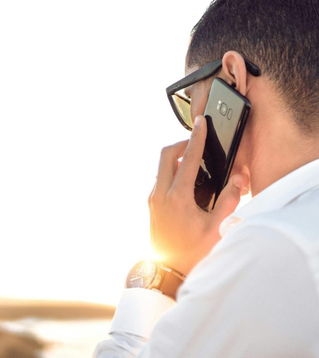 pexels-photo-804065-804065 Man outdoors in Morocco talking on smartphone, wearing sunglasses and white shirt, backlit by sunset.